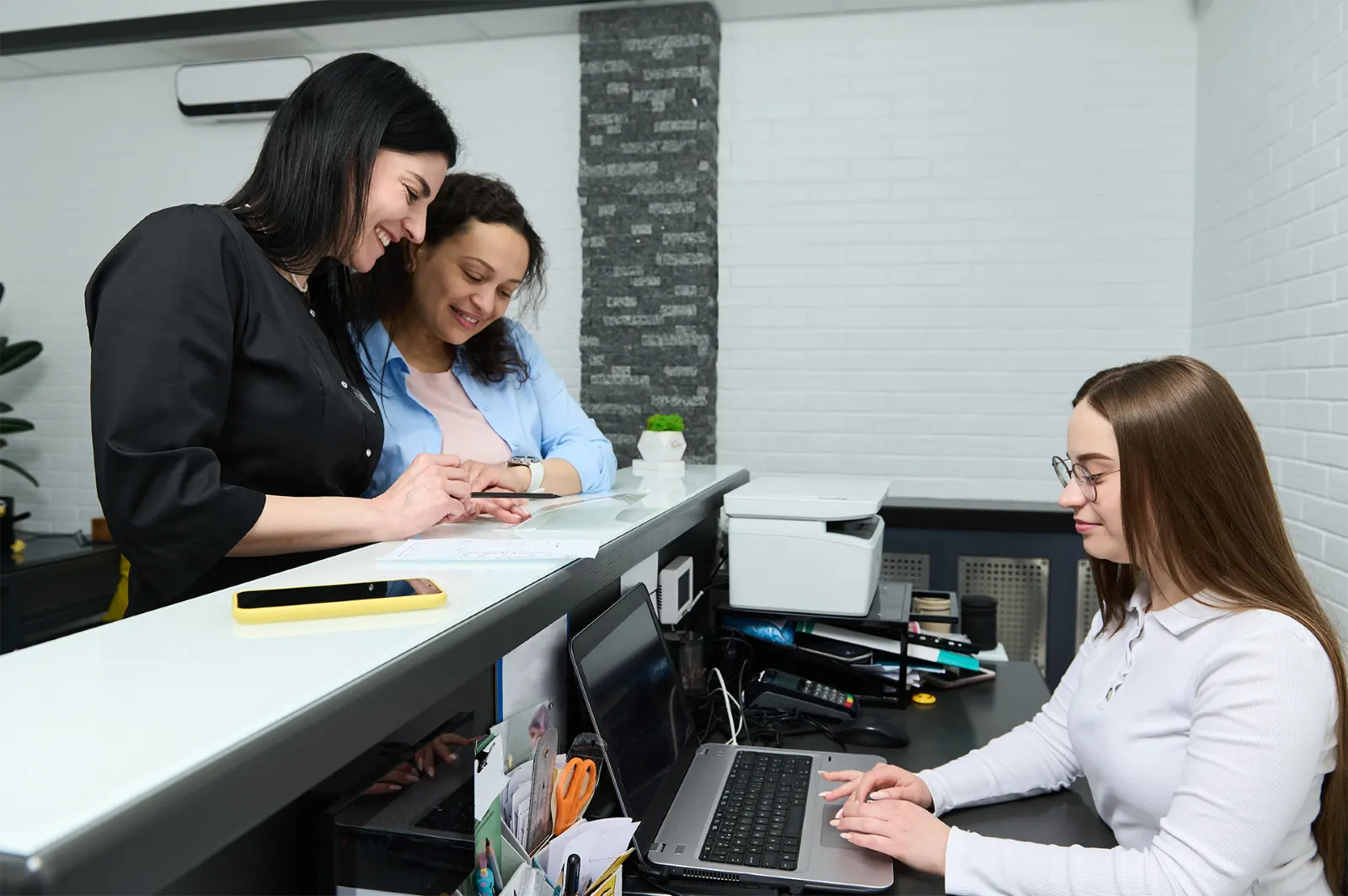 Two women checking into a busy clinic with a receptionist. h
