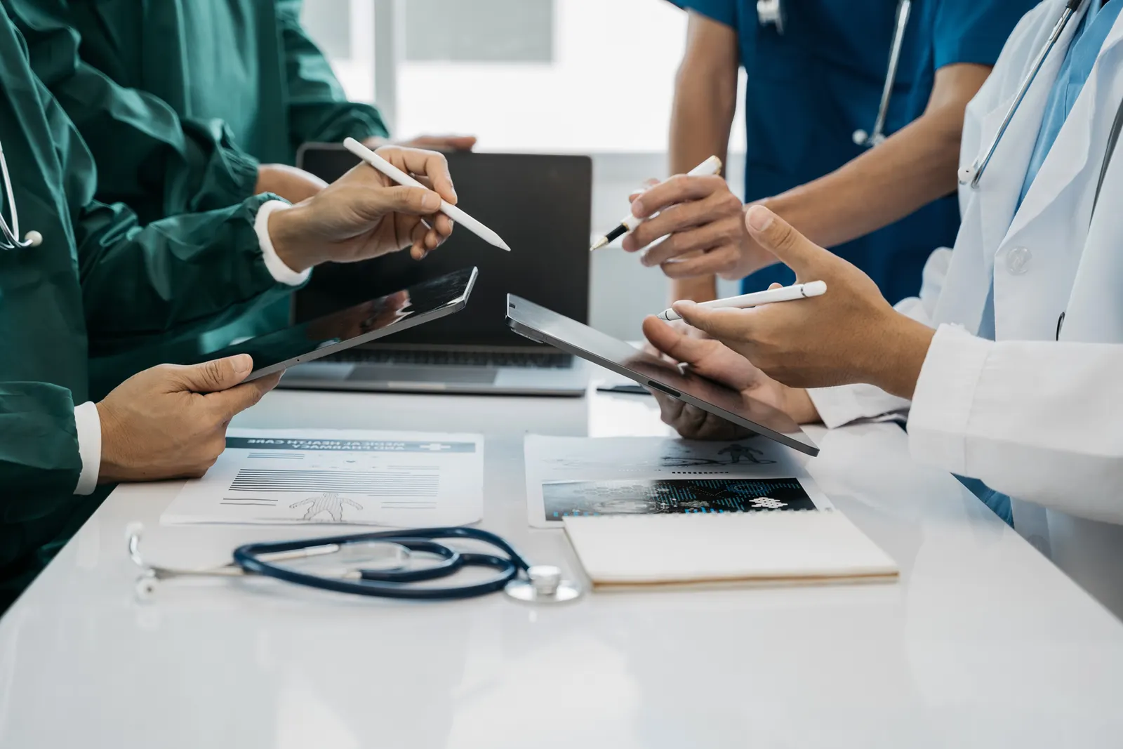A medical team of four coming together with laptops, and tablets to solve a problem.