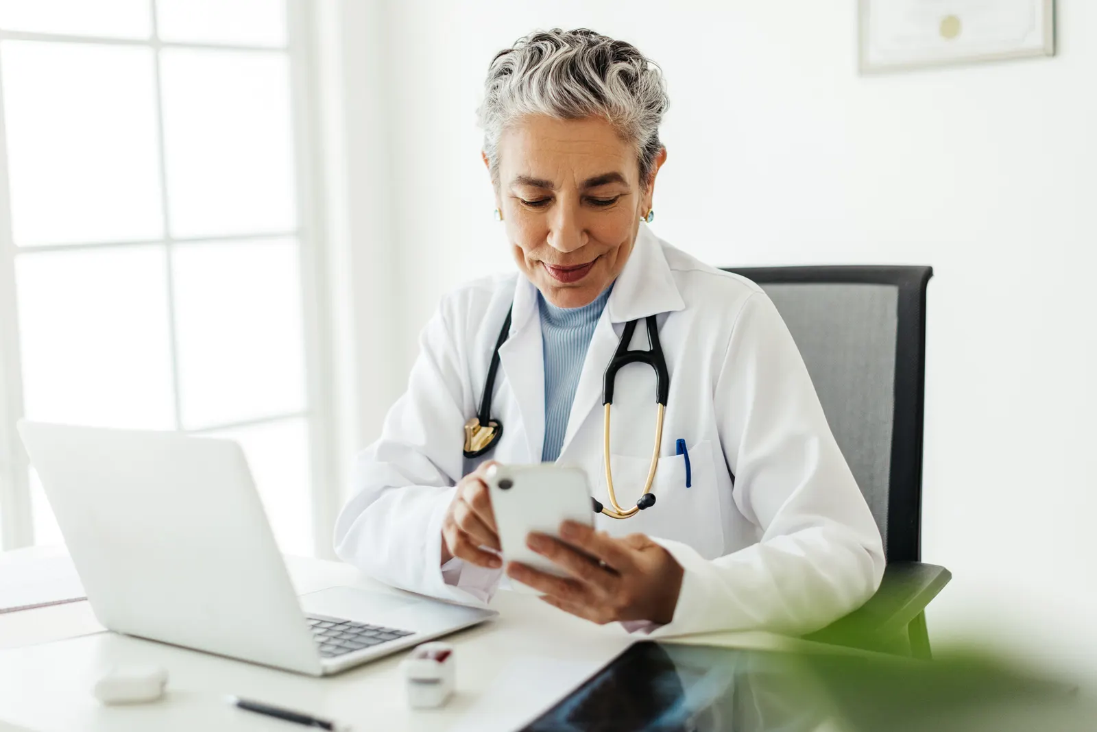 Wise looking woman doctor checking their smartphone in a white office. 