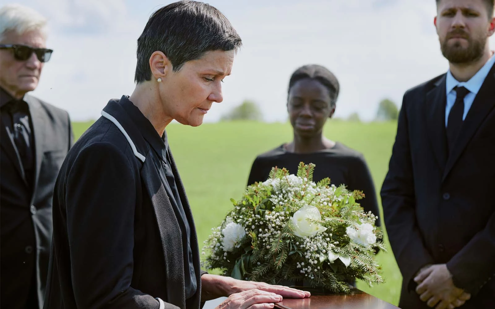 A family gathered at a graveside service, one woman resting her hand on the casket